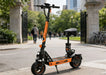 Orange electric scooter on a city street with people and bicycles in the background