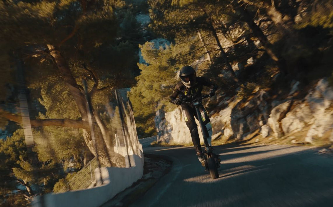Person riding a Teverun Fughter Supreme Ultra electric scooter  on a mountain road with trees and rocks.