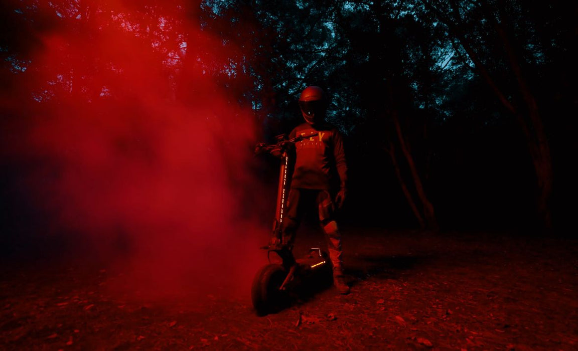 Person on a Teverun Fughter Supreme Ultra electric scooter  with red smoke in a dark forest setting