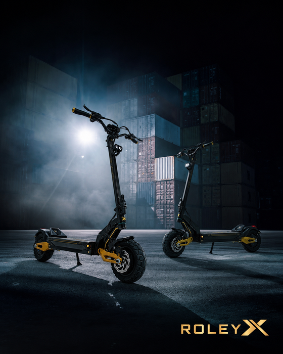 Two black and yellow ROLEYX electric scooters displayed in a moody, dark industrial setting with dramatic lighting and a stack of shipping containers in the background.