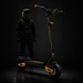 Person wearing a helmet and dark clothing standing next to a black and yellow scooter on a dark background